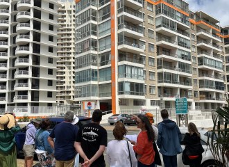 A group of people stands in front of a 1970s apartment building.